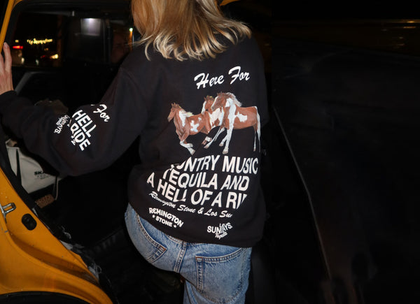 Person wearing a black sweatshirt with text and graphics, standing next to a yellow vehicle at night.