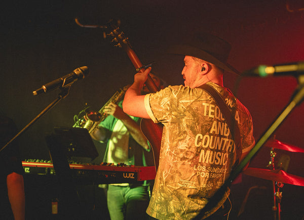 Person playing guitar on stage with a microphone and equipment.